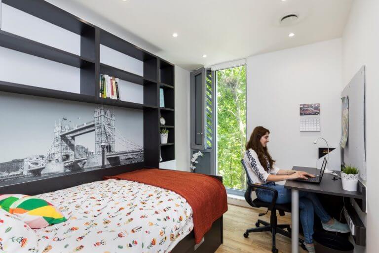 St Pancras en-suite bed area, with a bed, black shelves, a table and chair.