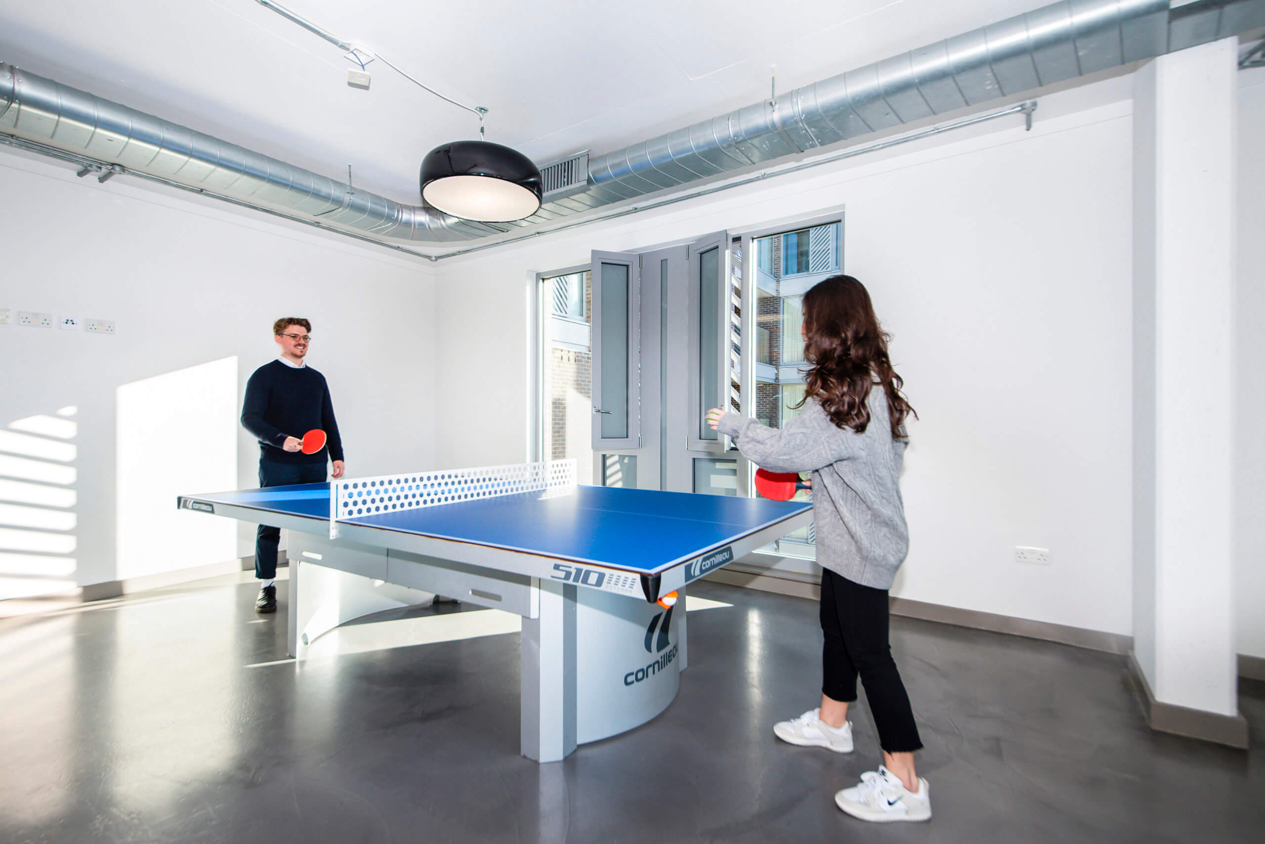 Two people playing at the ping pong table in a white rec room