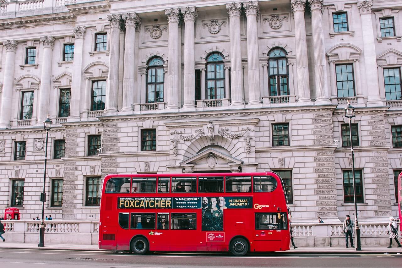 A double decker bus in London parked in front of a historical building.