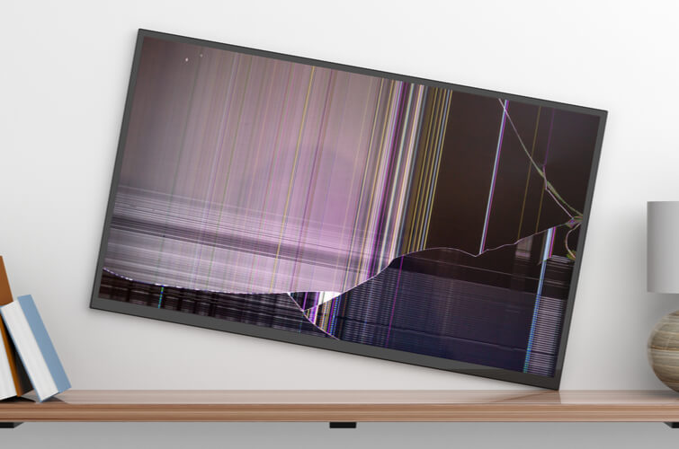 A broken television falling off the wall being held up by a wooden bookshelf against a white wall