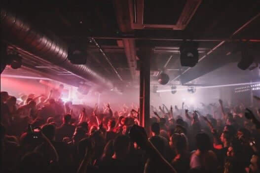 An in-crowd view of XOYO, with red lights, crowds of people, and an industrial feel to the design.
